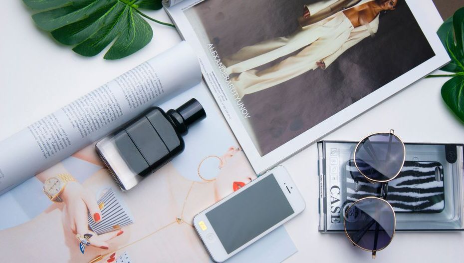 Flat lay of fashion items including sunglasses, perfume, and a magazine on a white surface.